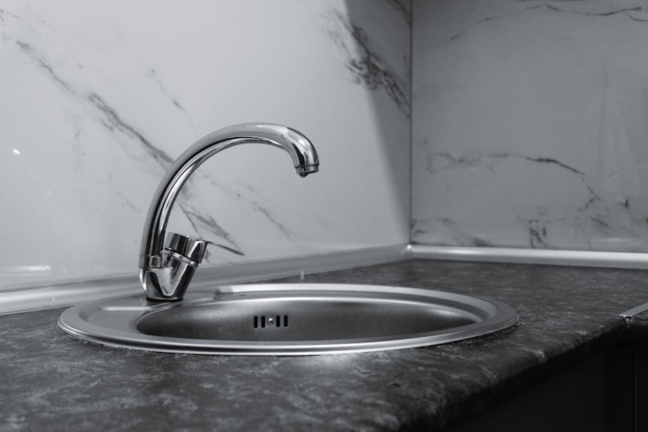 A stylish stainless steel kitchen faucet with a sleek and modern design set against a marble backsplash.